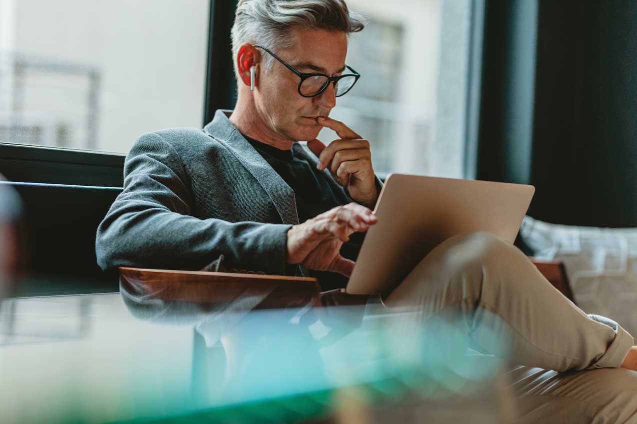 A man sat with his legs crossed analysing a laptop screen